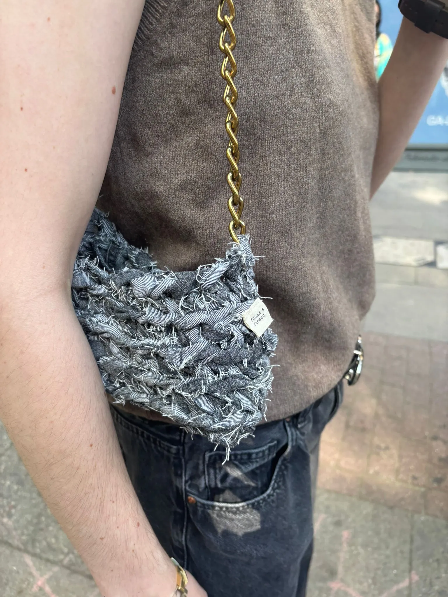 Kleine graue Denim-Häkeltasche mit goldener Kette, über der Schulter getragen