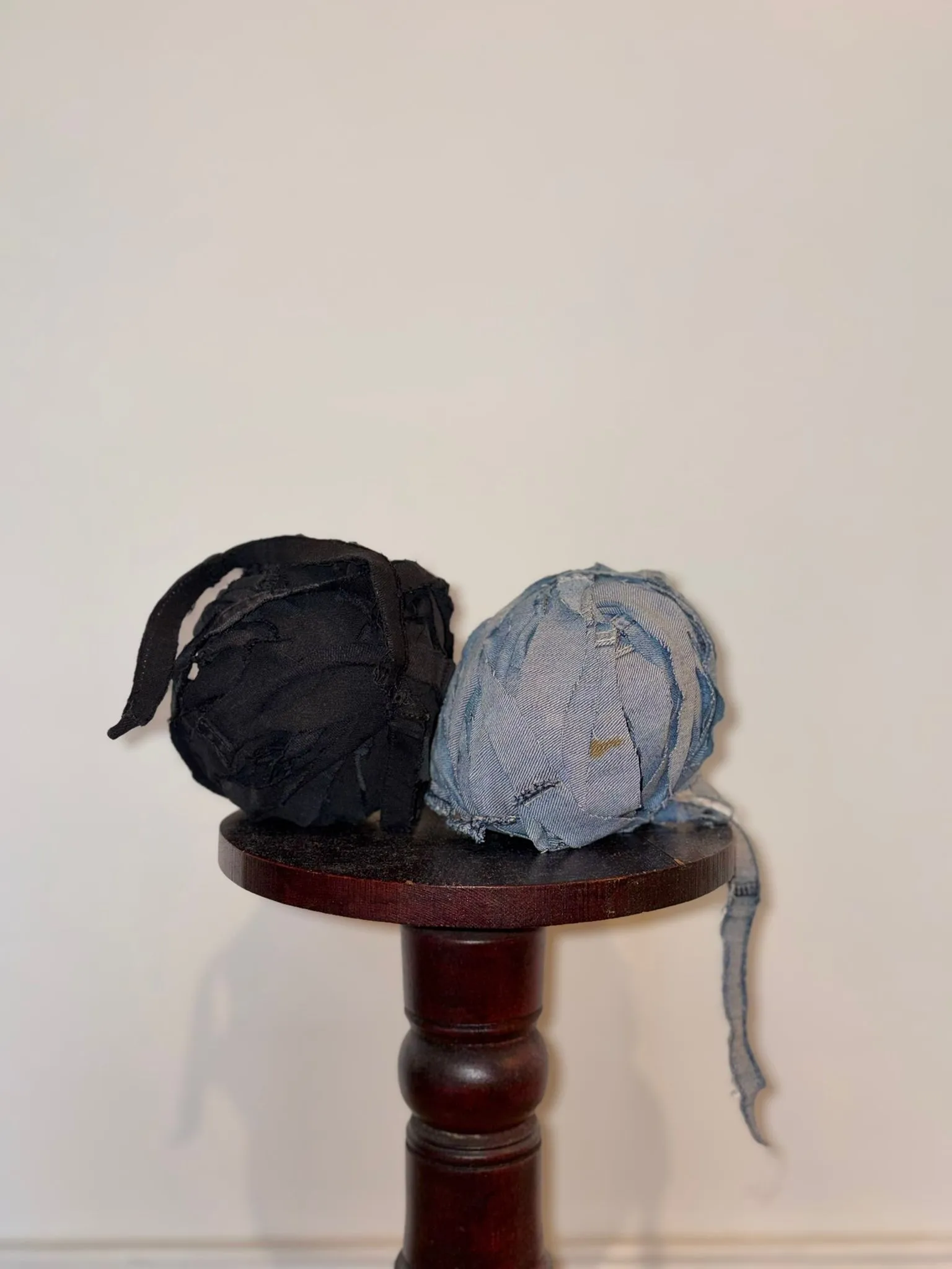 Zwei Garnknäuel aus geschnittenen Jeans-Streifen in Schwarz und Hellblau auf einem Holzhocker