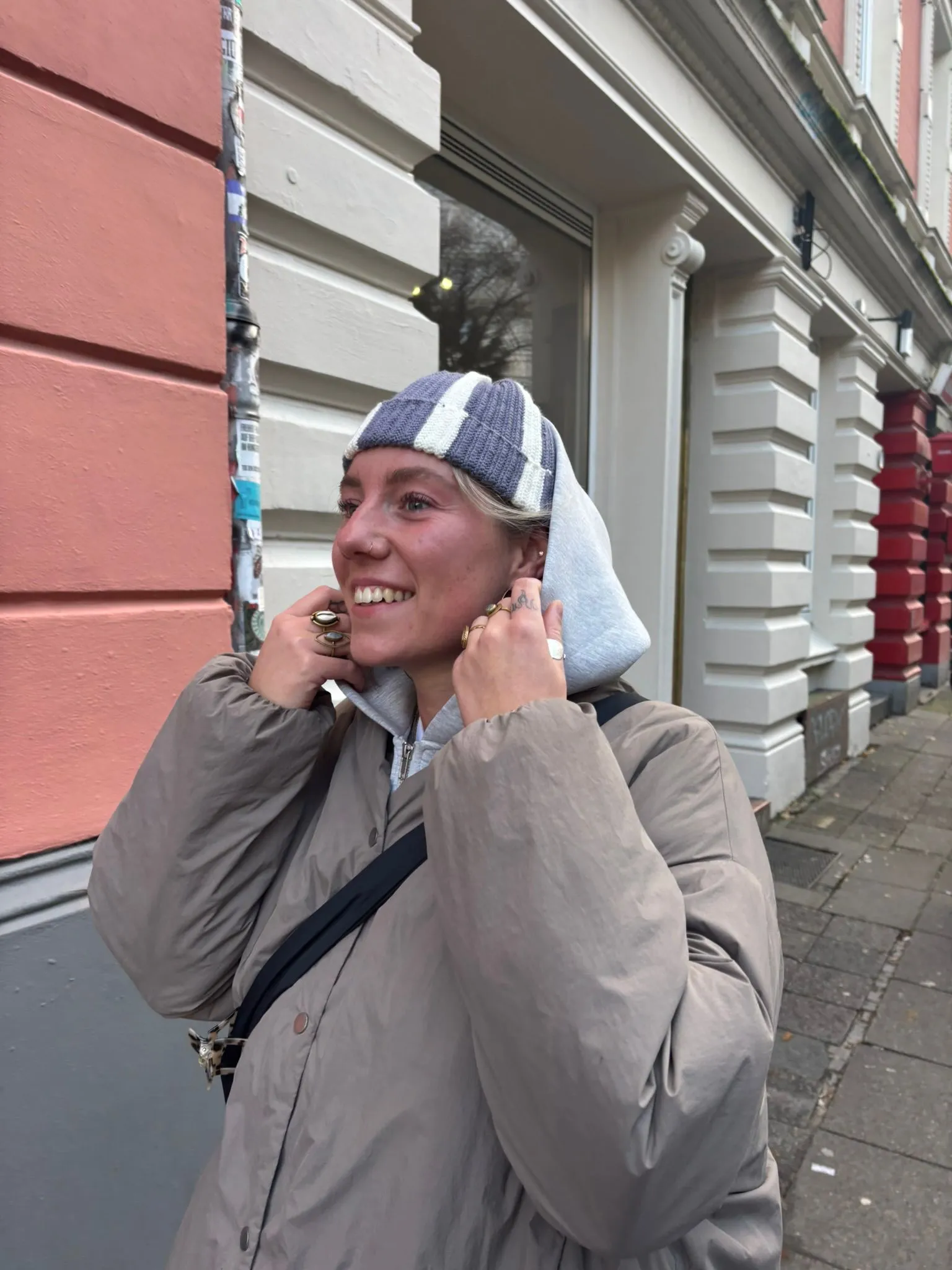 Jenny lacht auf der Straße in Hamburg, mit gehäkelter Mütze in Grau und Weiß