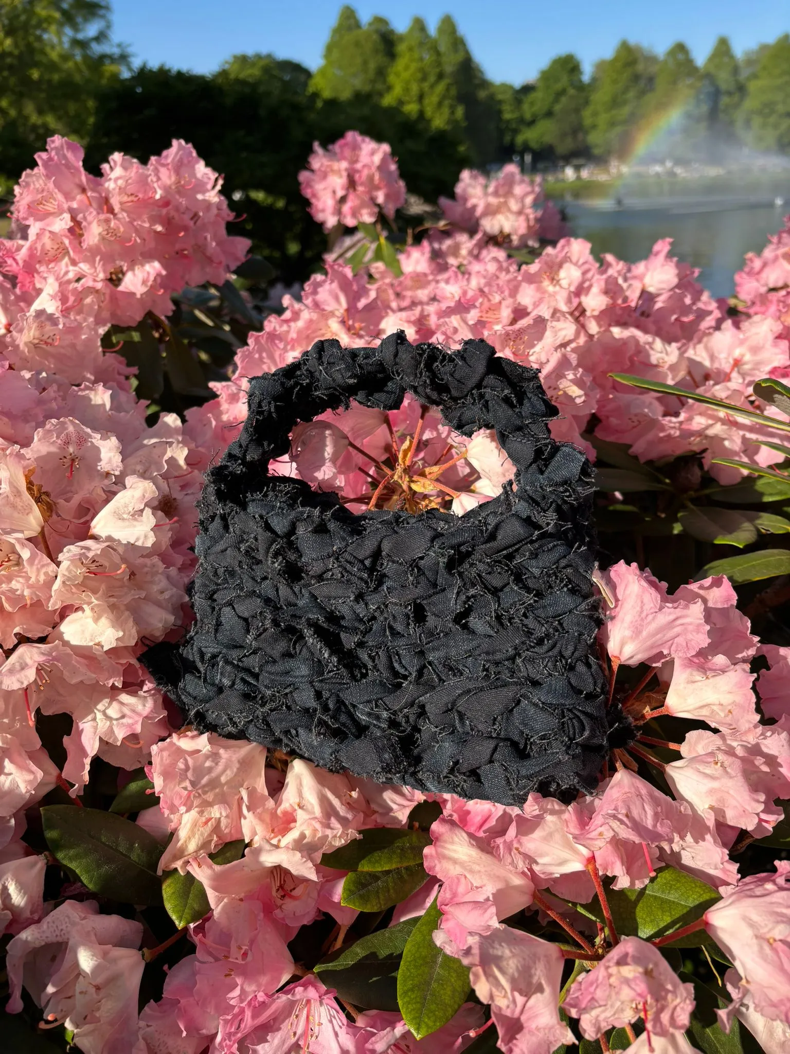 Schwarze strukturierte Häkeltasche aus Stoffstreifen eines alten Sitzbezugs, zwischen rosa Blüten